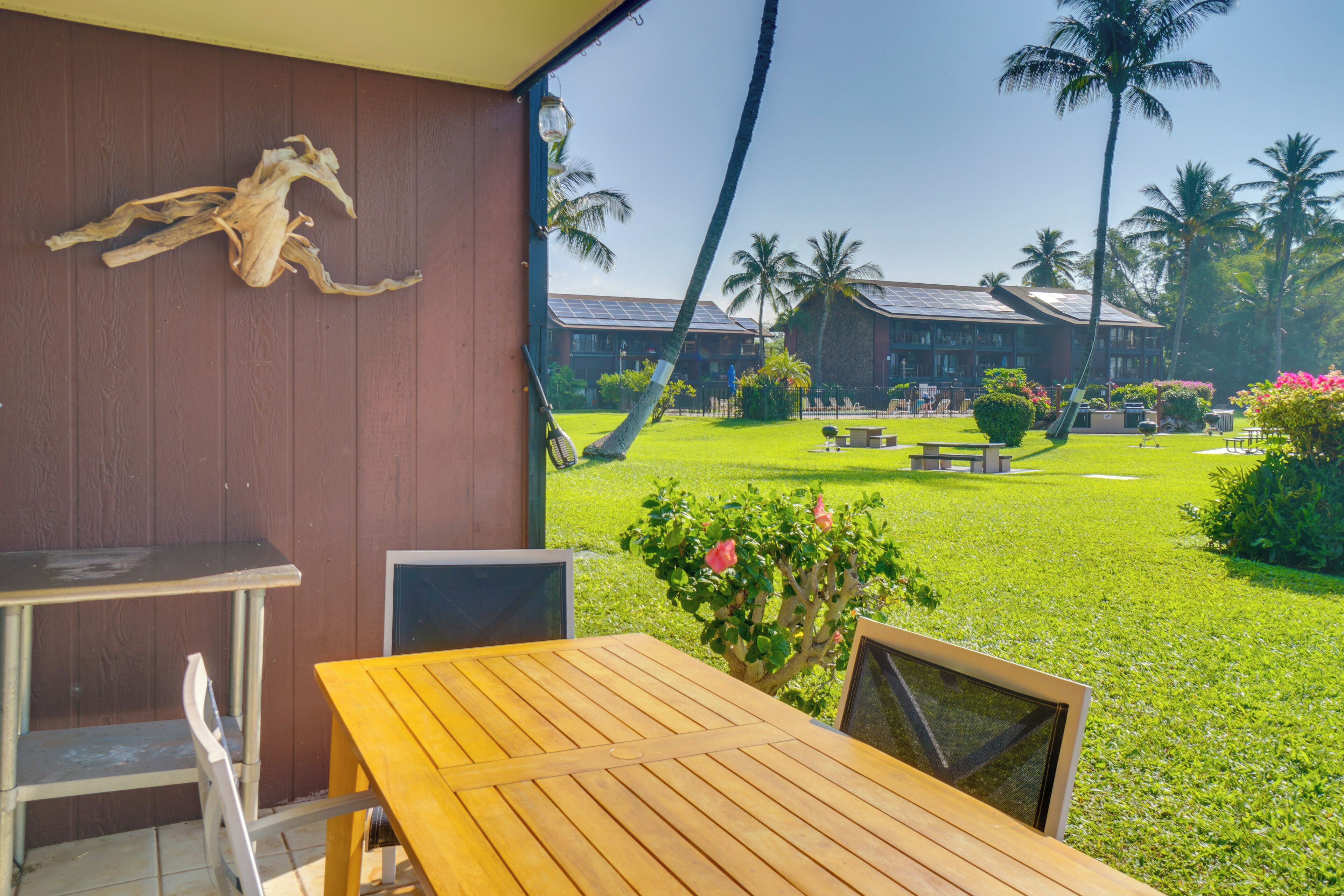 A wooden table and chairs in a covered outdoor area with a view of a golf course and a building with solar panels.