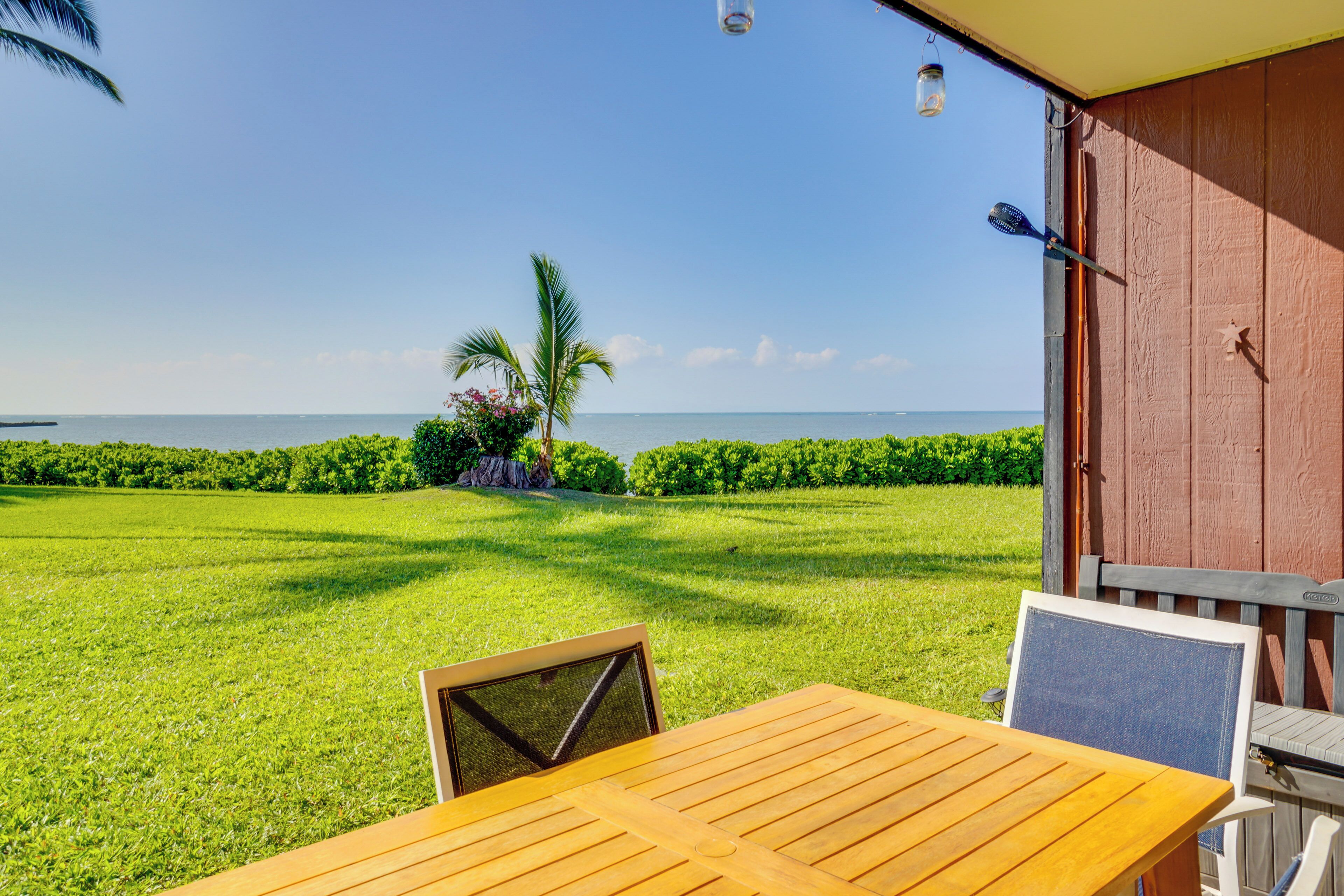 A wooden table and chairs in a sunny outdoor area with a view of the ocean.