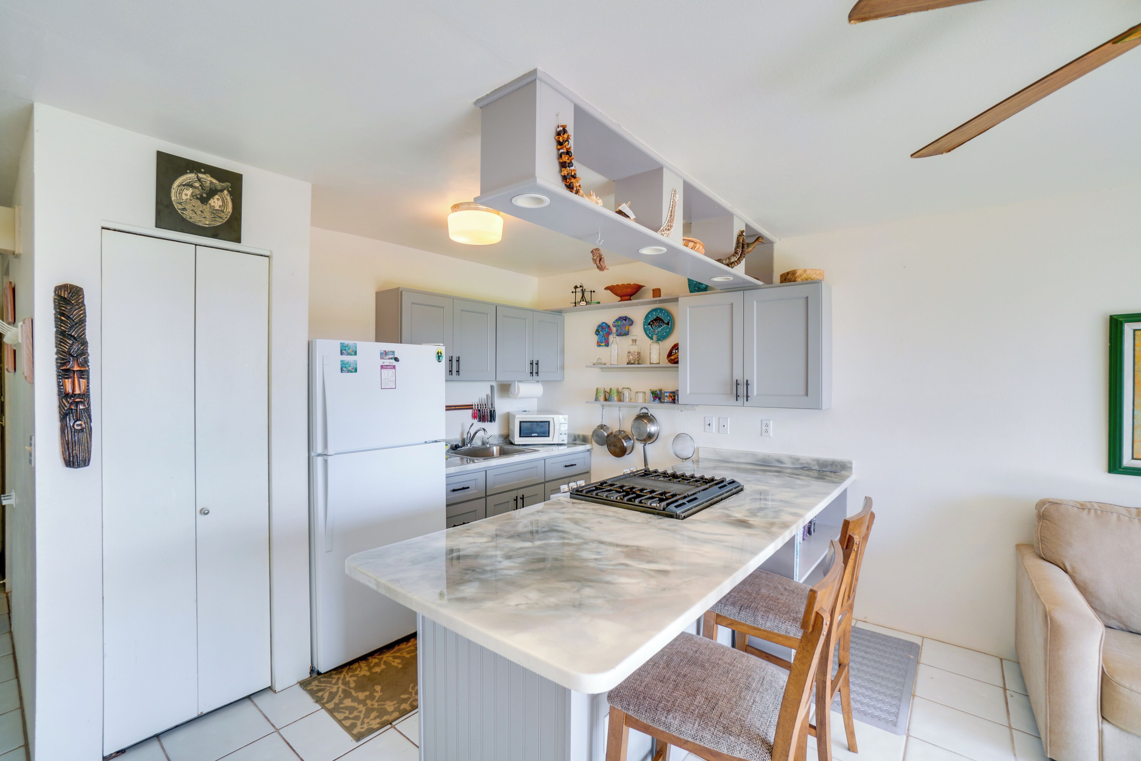 A modern kitchen with white cabinetry, a marble island, and a dining area with chairs.
