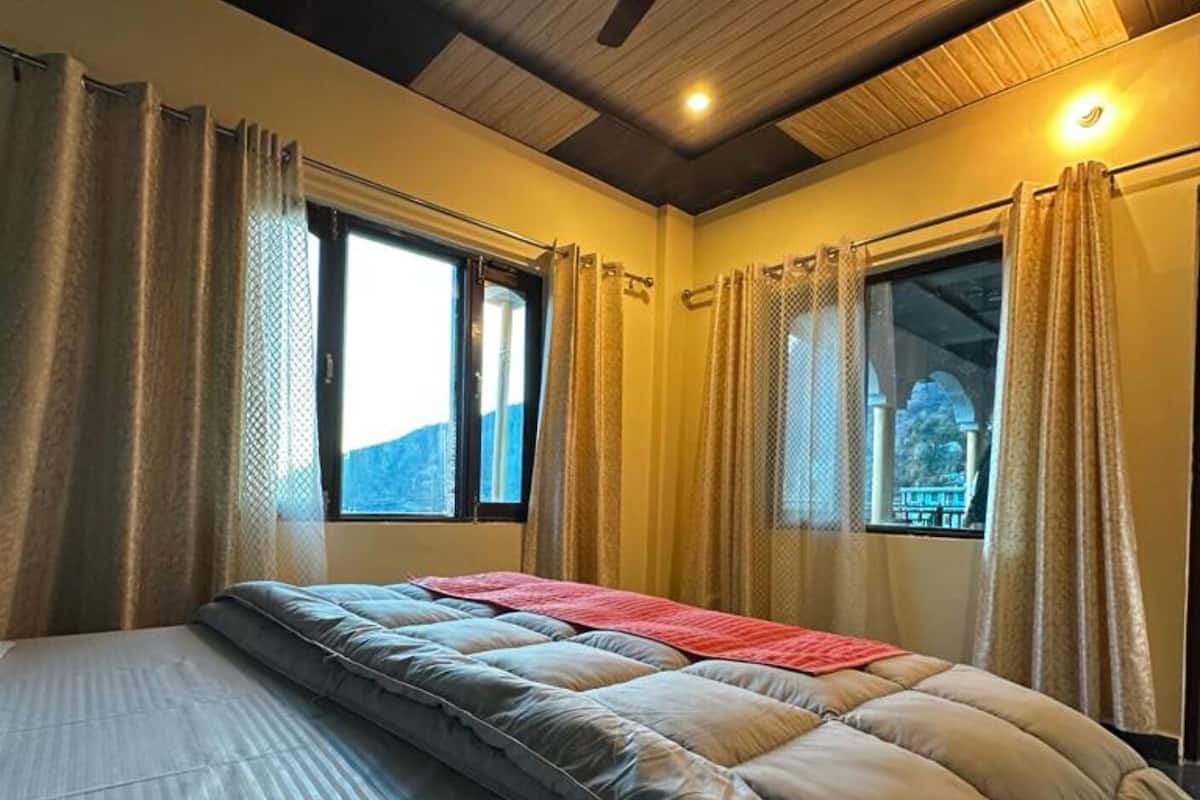 A bedroom with a large bed, two windows with curtains, and a wooden ceiling.