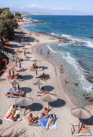 A beach with clear waters, umbrellas, and people sunbathing. - Villa Melia bythe beach Thalasses villas by Domisi (Rethymno)