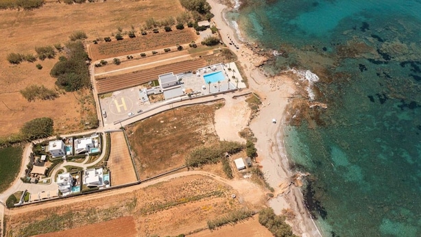 Vista aérea de una propiedad costera con piscina, helipuerto y campos adyacentes.