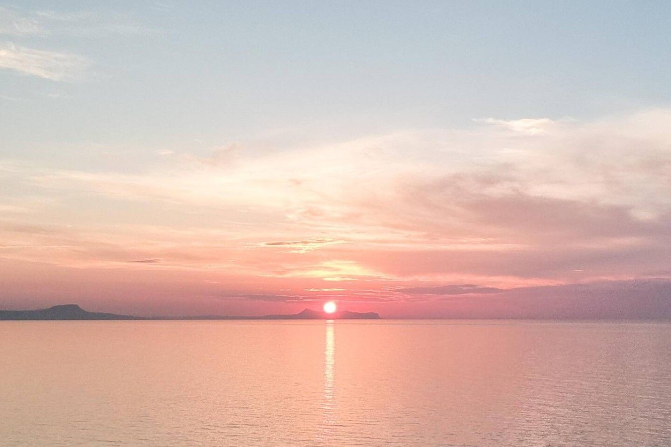Un atardecer sobre una superficie acuática tranquila con una masa de tierra distante.