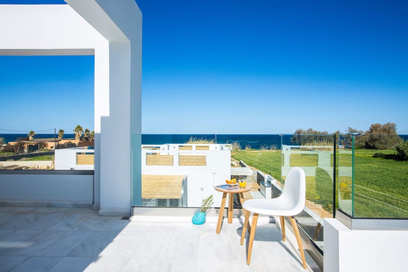 A modern balcony with a clear view of the sea, a table with a chair, and a glass railing.