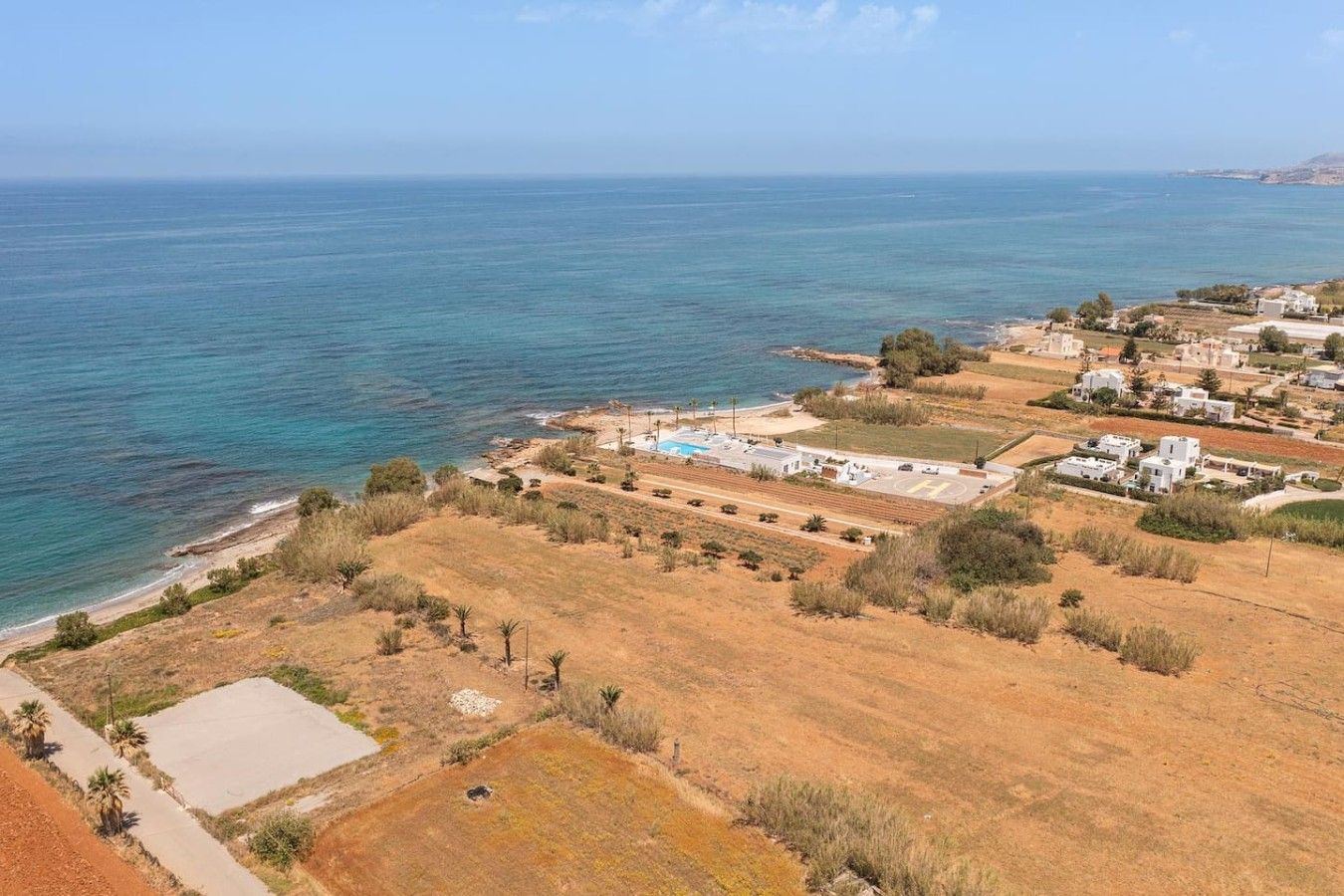 A coastal residential area with houses, a parking lot, and a clear view of the sea.