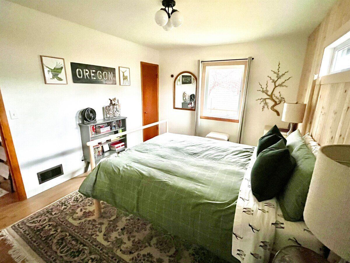 A bedroom with a bed, a bookshelf, a mirror, and a window.