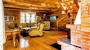 A cozy log cabin interior with a wooden floor, a dining table, a sofa, and a fireplace. - In The Woods Lodge With hot tub Inside Puszcza Knyszyśnka - Two-bedroom Villa (Suprasl)