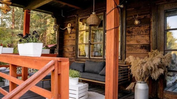 A rustic wooden cabin with a porch, a cushioned seating area, and potted plants. - In The Woods Lodge With hot tub Inside Puszcza Knyszyśnka - Two-bedroom Villa (Suprasl)