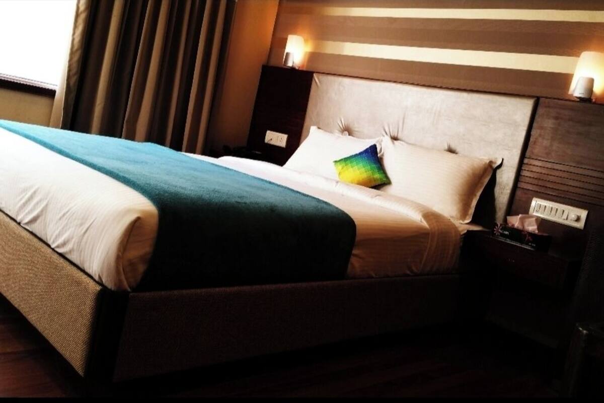 Una cama bien hecha con cabecera a rayas, una mesita de noche con lámpara y una ventana con cortinas.