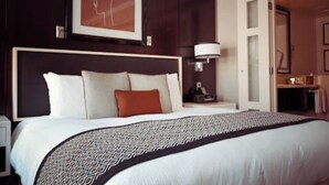 Une chambre d’hôtel avec un grand lit, une tête de lit, une table de chevet, une lampe et un tableau encadré au mur.