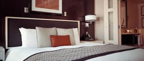 Habitación de hotel con una cama grande, cabecero, mesita de noche, lámpara y un cuadro en la pared.
