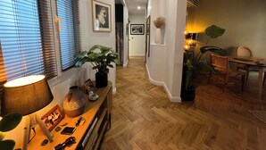 Un pasillo con suelo de madera, una zona de comedor con mesa y sillas, y una planta a la izquierda.