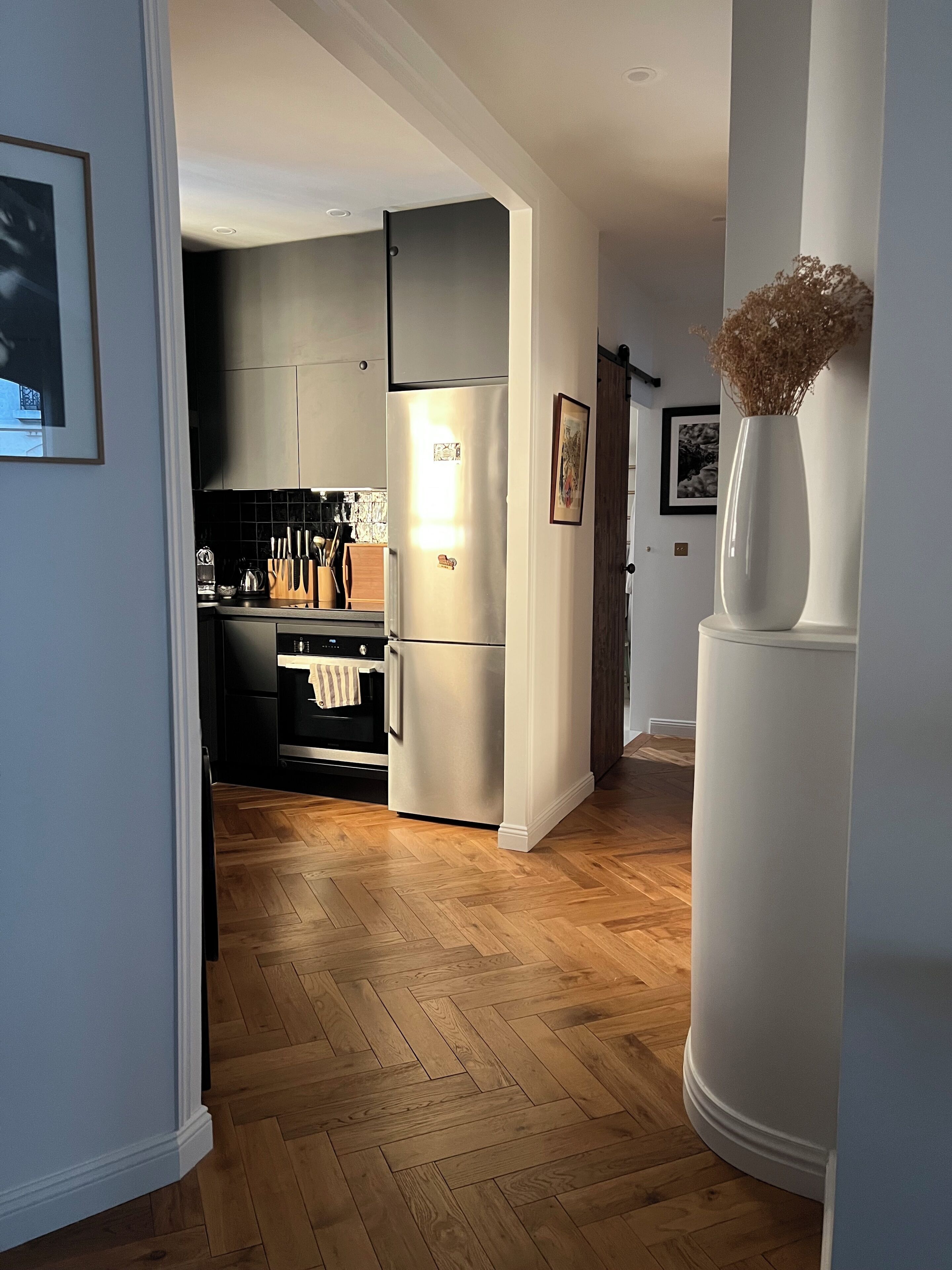 A modern kitchen with a refrigerator, oven, and wooden herringbone flooring.