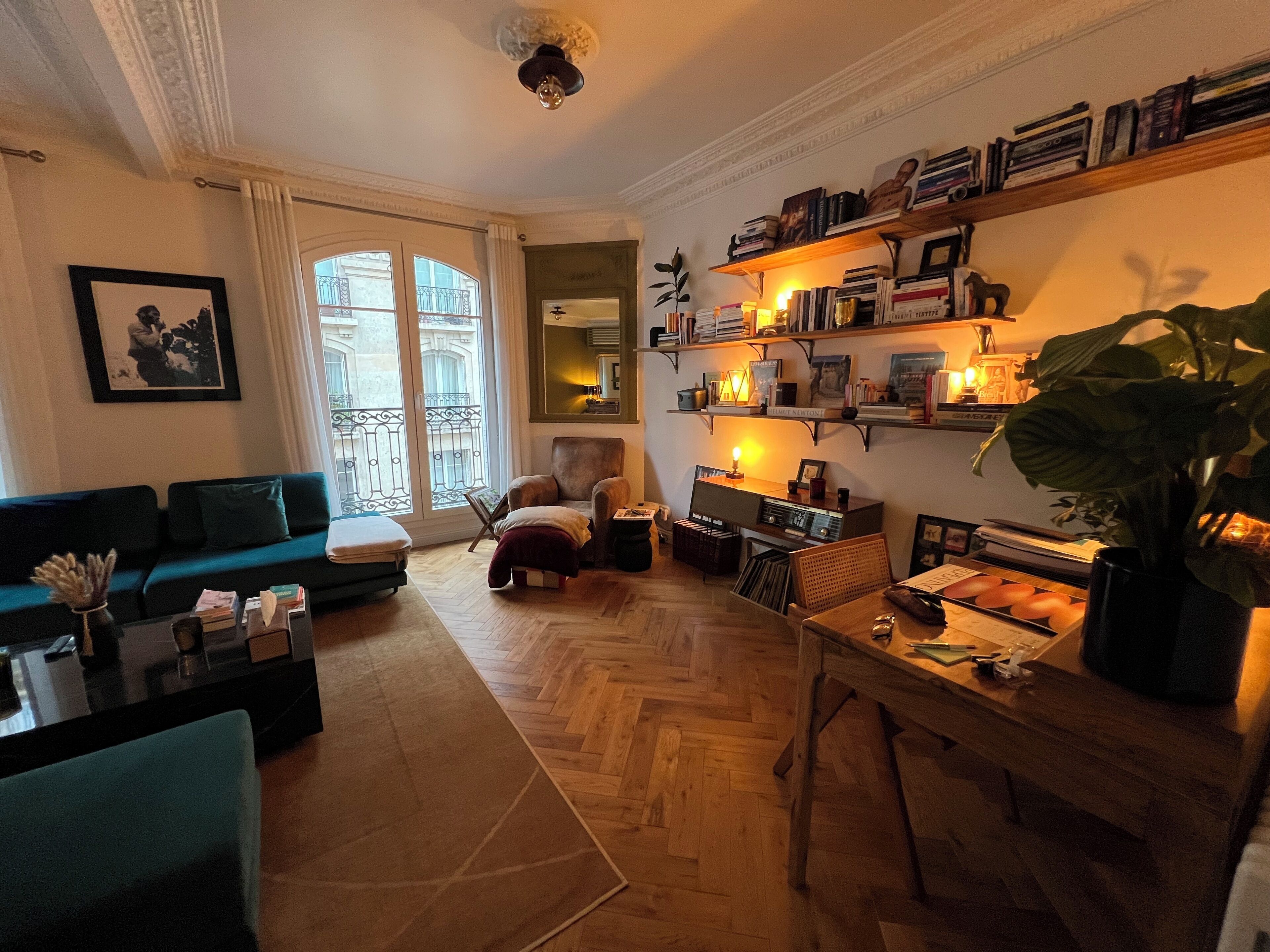 En stue med sofa, lænestol og sofabord. Reoler med bøger og en plante står i rummet.