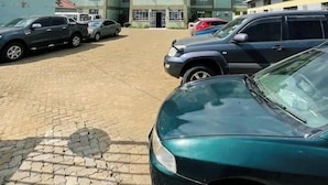 Ein Hotel mit mehreren Etagen und Balkonen, ein gepflasterter Parkplatz mit verschiedenen Autos und ein klarer Himmel mit vereinzelten Wolken.