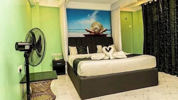 Ein Schlafzimmer mit einem Bett, einem Ventilator, einem Nachttisch und einem Wandbild.