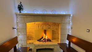 Una chimenea de piedra con fuego, flanqueada por bancos de madera y un pequeño árbol de Navidad en la parte superior.