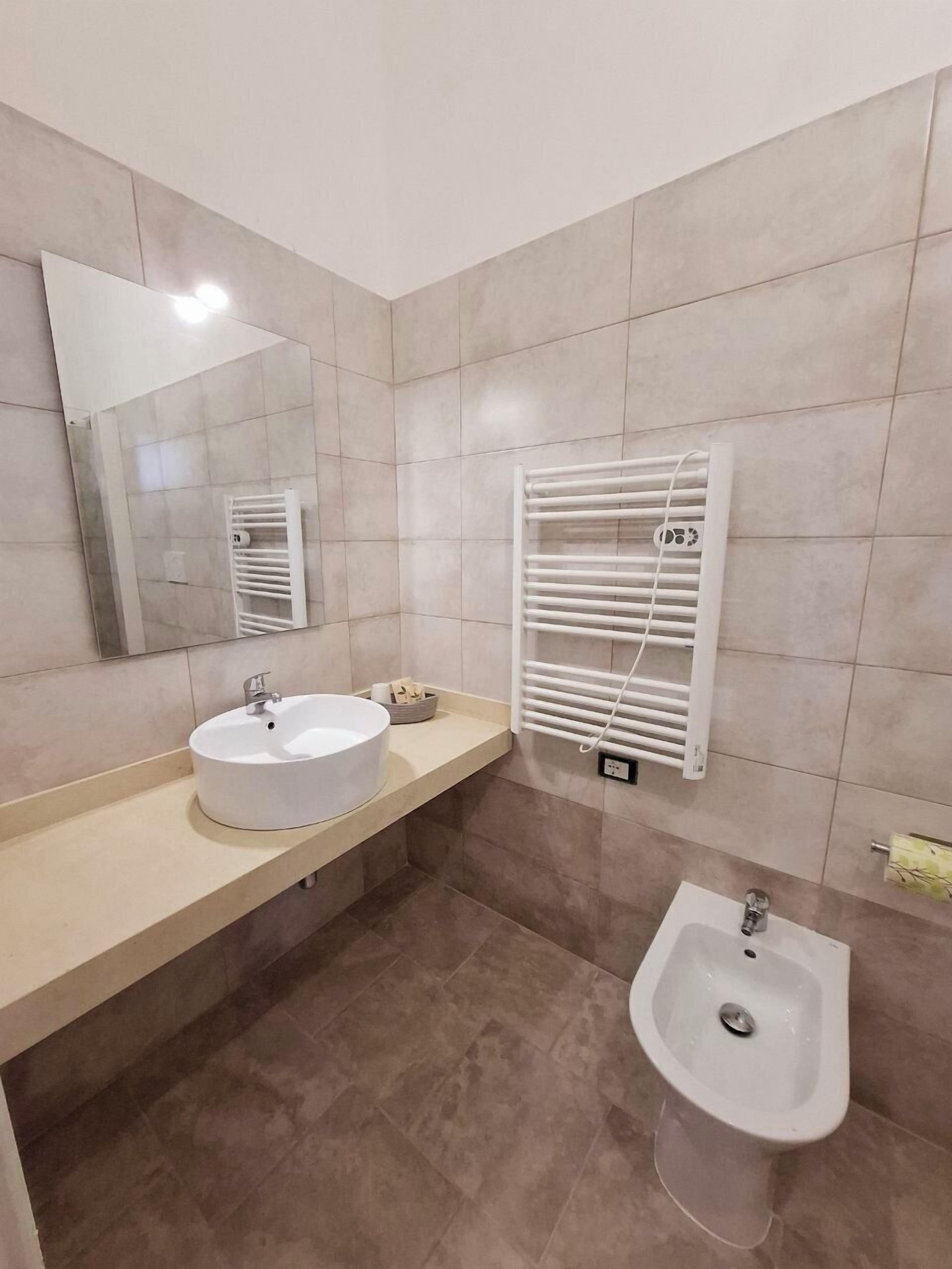A bathroom with a round sink, a bidet, a towel rack, and a mirror.