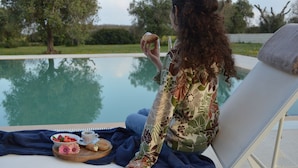 Una persona relajándose junto a la piscina, disfrutando de una bebida y aperitivos.