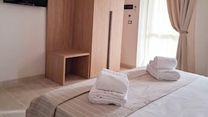 Habitación de hotel con cama, armario de madera, televisor de pantalla plana en la pared y ventana con cortinas.