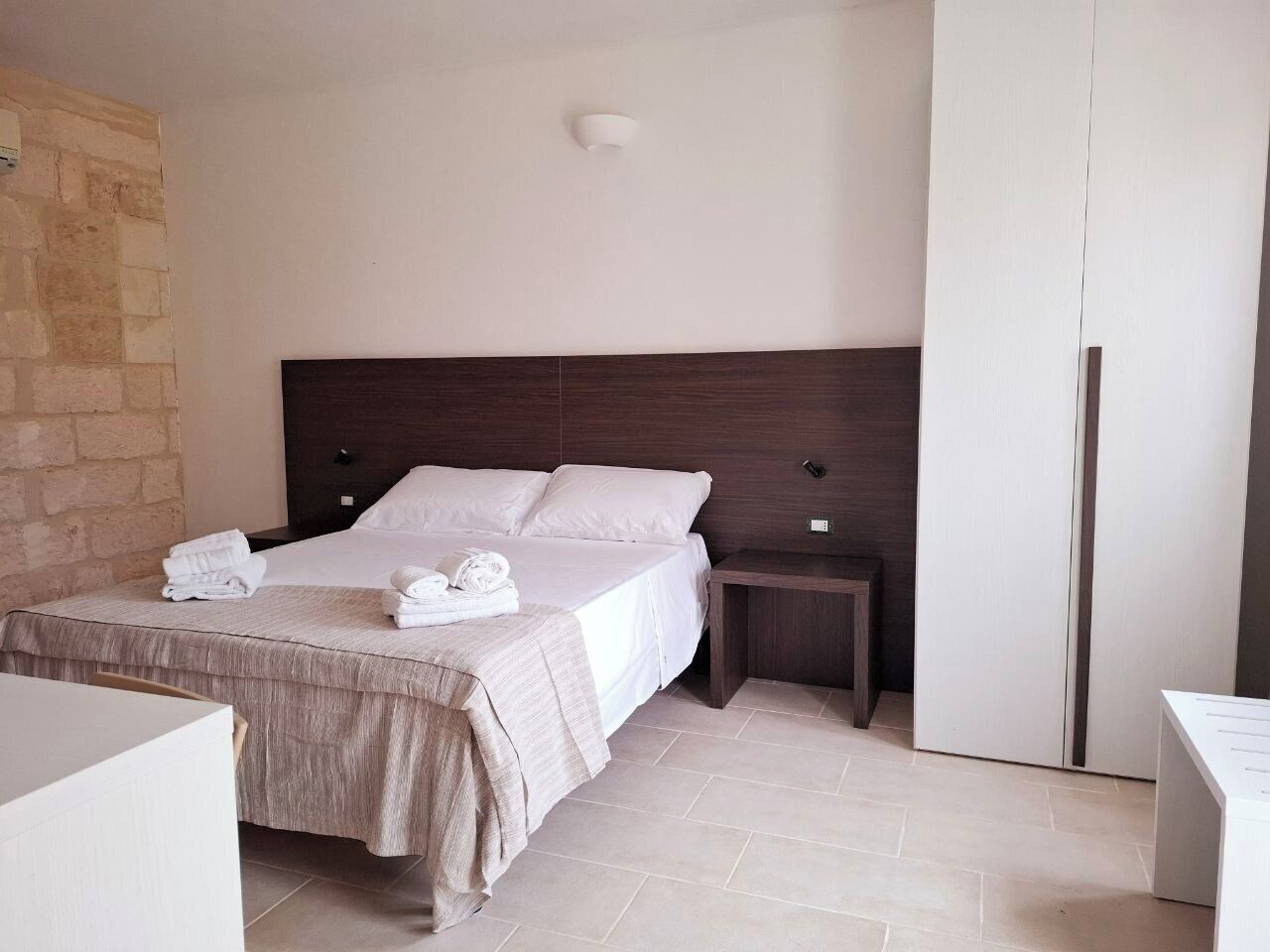 Une chambre d’hôtel moderne avec un grand lit, une table de chevet, une armoire et un mur en pierre.
