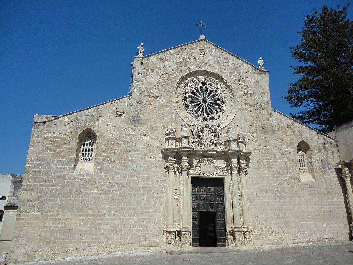Una iglesia de piedra con un gran ventanal circular, una puerta negra y dos estatuas en el tejado.