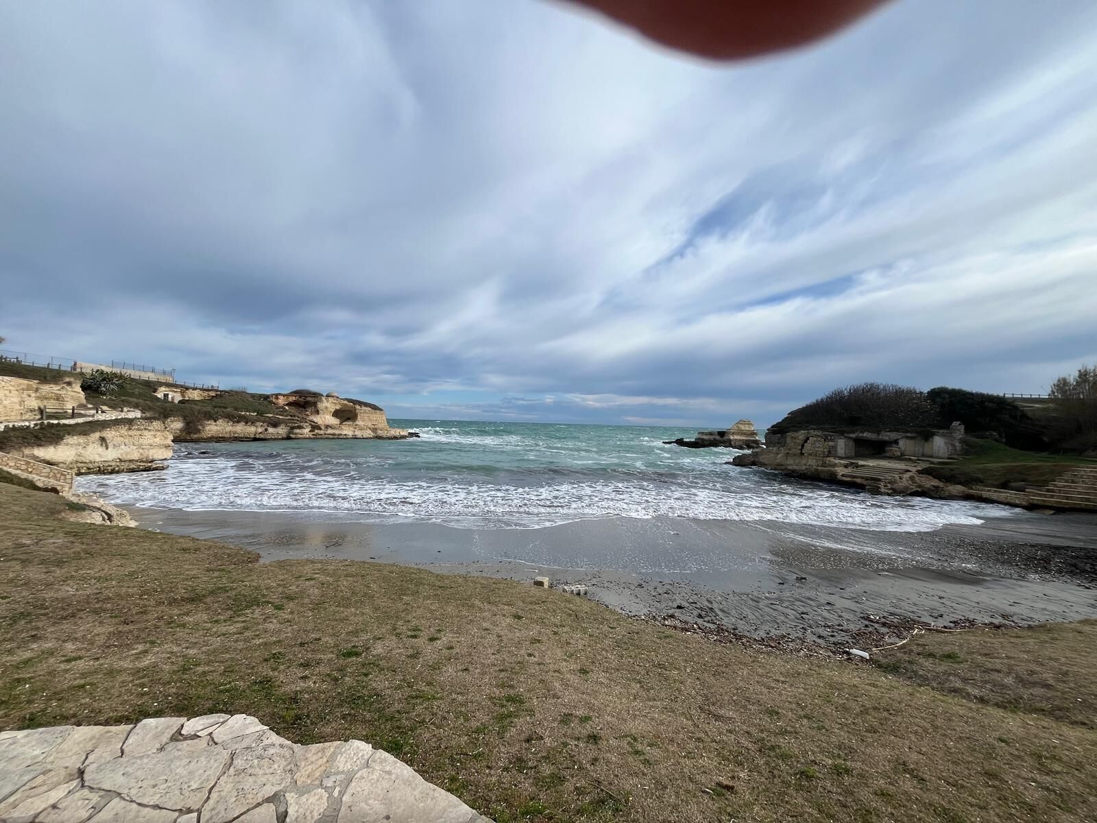 Un paisaje costero con acantilados rocosos, una playa de arena y un mar tranquilo bajo un cielo nublado.