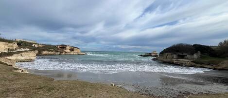 Un paisaje costero con acantilados rocosos, una playa de arena y un mar tranquilo bajo un cielo nublado.