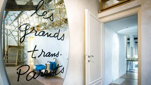 A hallway with a large mirror reflecting a room with a ladder, a chair, and a blue towel.