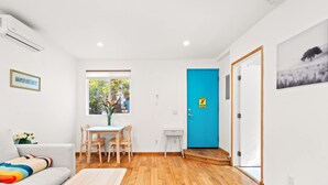 A modern living room with a sofa, a dining table with chairs, a small side table, and a blue door with a "Watch Your Step" sign. - Scenic Retreat With Deck Stunning Views in LA (Glendale)