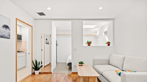 A modern living room with a sofa, a wooden coffee table, and a small side table. There is a hallway leading to a bedroom with a bed and a bathroom. - Scenic Retreat With Deck Stunning Views in LA (Glendale)