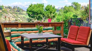 An outdoor patio with a wooden bench, a table, and chairs. There is a view of a mountainous landscape in the background. - Scenic Retreat With Deck Stunning Views in LA (Glendale)