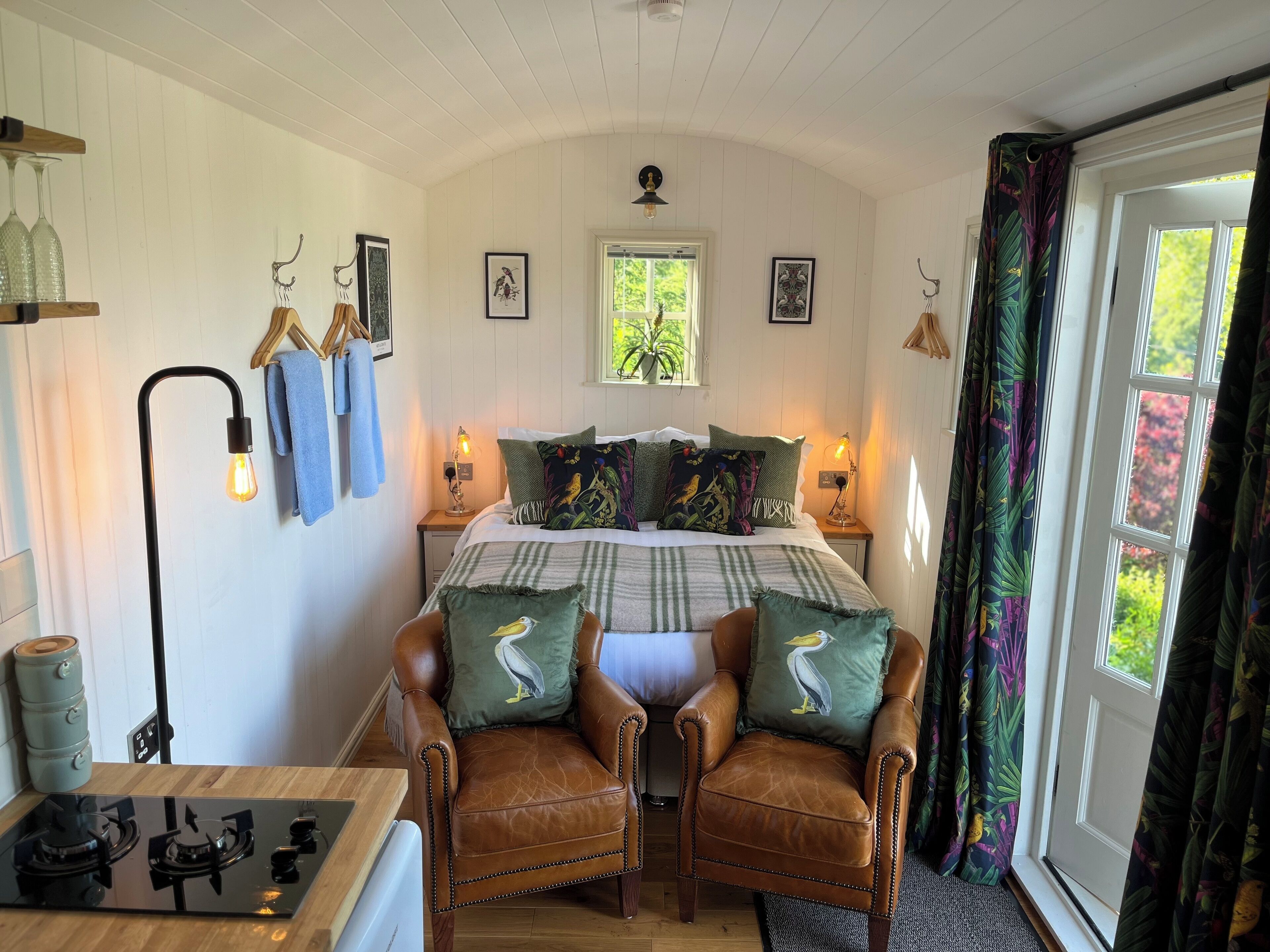 A cozy bedroom with a bed, two chairs, a window, and a nightstand with lamps.