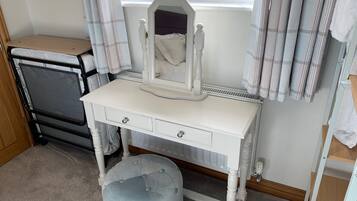 Une coiffeuse blanche avec un miroir, un petit tabouret et une fenêtre avec des rideaux.