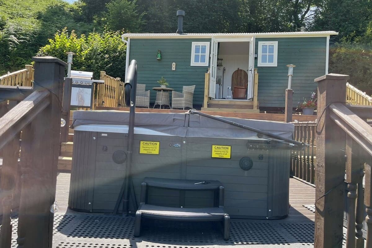 Un espace avec un bain à remous, agrémenté de panneaux d’avertissement, une terrasse en bois et, au fond, un bâtiment vert.