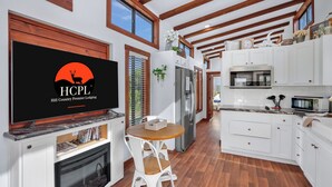 A modern kitchen with white cabinets, a built-in oven, and a large TV displaying a logo. - Pet-Friendly Farmhouse Tiny Home w/ Private Deck (Lampasas)