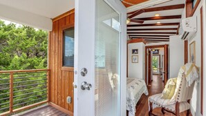 A wooden balcony with a glass door leading to a bedroom with a bed and a chair. - Pet-Friendly Farmhouse Tiny Home w/ Private Deck (Lampasas)
