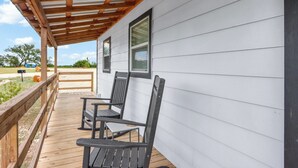 A covered porch with wooden railings and two dark-colored chairs.