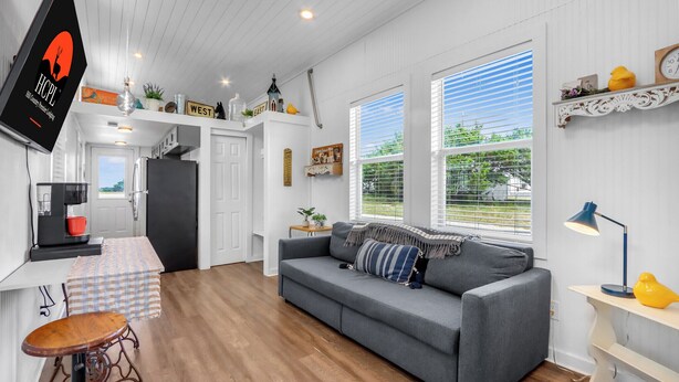 A modern kitchen with white cabinetry, a dining area with a checkered tablecloth, and a gray sofa with a striped pillow.