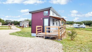 A small, single-story cabin with a wooden deck and a gravel driveway.