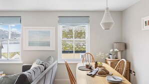 A modern kitchen with a wooden dining table, chairs, and a hanging light fixture. - Churchside Cottage - 2 bed in the heart of Fowey (Fowey)