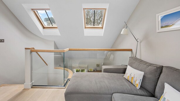 A modern loft bedroom with skylights, a glass staircase, and a grey sofa. - Churchside Cottage - 2 bed in the heart of Fowey (Fowey)