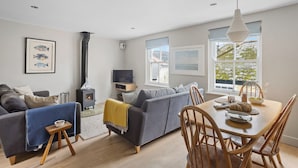 A modern living room with a sofa, a dining table with chairs, a fireplace, and large windows. - Churchside Cottage - 2 bed in the heart of Fowey (Fowey)