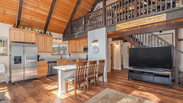 A spacious kitchen with wooden cabinets, a stainless steel refrigerator, and a dining area with a large TV and wooden chairs.