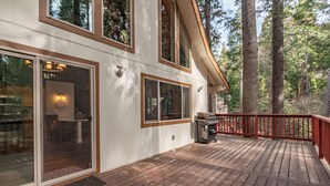 A wooden deck with a red railing, a barbecue grill, and a dining area with a table and chairs.