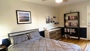 A bedroom with a bed, a ceiling fan, a bookshelf, and a desk.