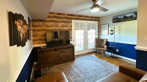 A living room with a TV, a ceiling fan, a chair, and a couch.
