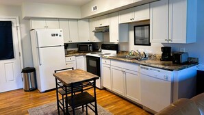 A compact kitchen with white cabinets, a microwave, a stove, and a dishwasher. There's a small dining table with two chairs.