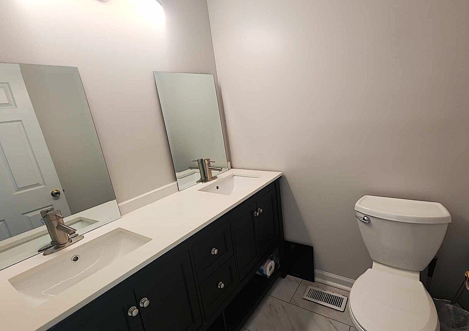 A bathroom with two sinks, a toilet, and a mirror.
