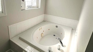 A bathroom with a large bathtub, a window, and a wall-mounted picture.